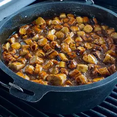 Leckere Currywurst-Stücke köcheln in einer würzigen Sauce in einem gusseisernen Dutch Oven auf dem Grill.
