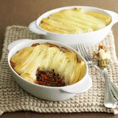 Zwei Auflaufformen mit goldbraunem Shepherd's Pie, bedeckt mit kunstvoll gespritztem Kartoffelpüree.