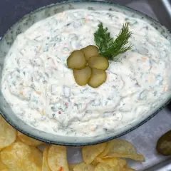 Cremiger blue cheese dip mit Dill und Gurkenscheiben, serviert mit Kartoffelchips und Gewürzgurken.