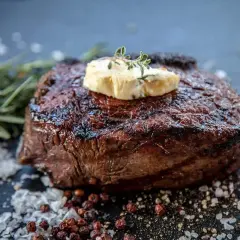 Perfekt gegrilltes Entrecôte mit Kräuterbutter, umgeben von grobem Salz und Pfefferkörnern. Ein Fest für Fleischliebhaber!