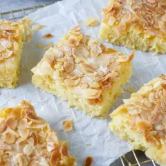 Saftiger Buttermilch Kuchen mit Mandelsplittern und Zucker bestreut, auf Backpapier und einem Gitter angerichtet.
