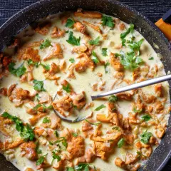 Pfifferlinge in cremiger Rahmsauce, garniert mit Petersilie, in einer Pfanne. Ein Löffel ragt aus der köstlichen Speise.