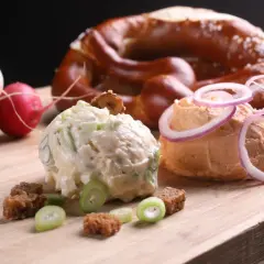 Zwei Portionen Obazda, garniert mit Zwiebelringen und Kräutern, daneben Radieschen und ein Brezel. Perfekt für ein Obazda Rezept!