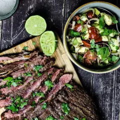 Perfekt gegrilltes Flanksteak, in Scheiben geschnitten, mit frischem Koriander und Limettenspalten, daneben ein bunter Salat.