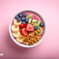 Ein farbenfrohes Acai Bowl Rezept mit Bananen, Erdbeeren, Blaubeeren, Kiwi und Granola auf rosa Hintergrund.