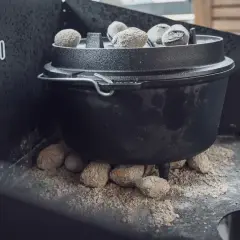 Ein Dutch Oven auf einem Gasgrill, bereit für ein köstliches Outdoor-Abenteuer. Glühende Kohlen sorgen für die perfekte Hitze.