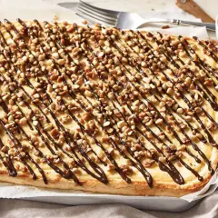 Ein rechteckiger "Friss dich dumm Kuchen" mit cremiger Füllung, garniert mit Nüssen und Schokoladensauce.
