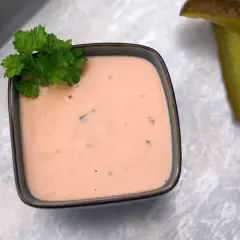 Cremige In-N-Out Burger Sauce in einer Schale, garniert mit Petersilie. Daneben liegen zwei saftige Gurkenscheiben.