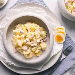 Ein cremiger Kartoffelsalat mit Mayonnaise, Schinken und Gewürzgurken, serviert mit gekochten Eiern. Ein klassisches Kartoffelsalat Rezept mit Mayonnaise.