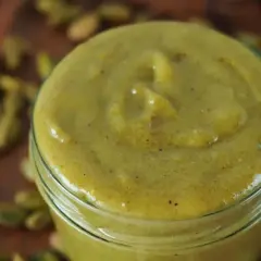 Selbstgemachte Pistaziencreme in einem Glas, umgeben von ganzen Pistazien. Perfekt zum Backen und Genießen.