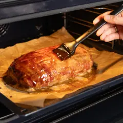 Ein Braten, umwickelt mit Bacon, wird im Backofen mit einer Glasur bestrichen. Die Bacon-Bomb-Zubereitung im Ofen ist fast fertig.