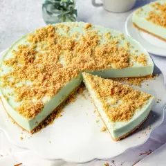 Eine cremige Philadelphia Torte Waldmeister mit knuspriger Streuselhaube, ein Stück ist bereits angeschnitten.