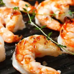 Saftige black tiger Garnelen grillen auf einer heißen Grillplatte, garniert mit frischem Thymian.