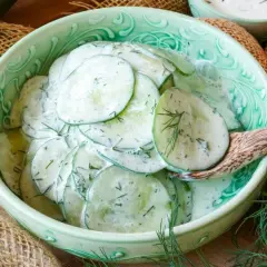 Frischer gurkensalat mit saurer sahne und Dill, serviert in einer grünen Schüssel mit einem Holzlöffel.
