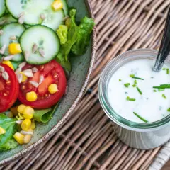 Frischer Salat mit Tomaten, Gurken und Radieschen neben einem Glas mit selbstgemachtem Joghurt-Dressing, garniert mit Schnittlauch.