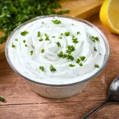 Cremige Sour Cream, frisch zubereitet, mit Schnittlauch garniert. Dazu Zitrone und ein Löffel – perfekt zum Sour Cream selber machen.