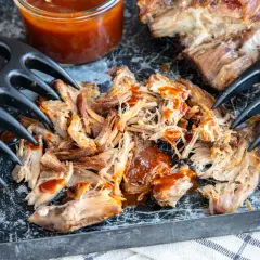 Zartes pulled pork sous vide, mit BBQ-Sauce beträufelt, bereit zum Zerreißen mit Fleischgabeln.