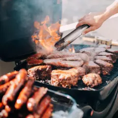 Fleisch und Würstchen brutzeln auf einem Grill auf dem Balkon. Die Frage, ob man auf dem Balkon grillen darf, wird hier mit Genuss beantwortet.