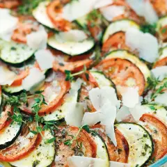 Schicht für Schicht ein Genuss: Ein köstlicher Tomaten Zucchini Auflauf, garniert mit Parmesan und frischen Kräutern.