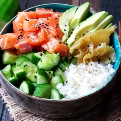 Eine bunte Sushi Bowl mit Lachs, Avocado, Gurke und Reis. Sesamkörner bestreuen die frischen Zutaten.