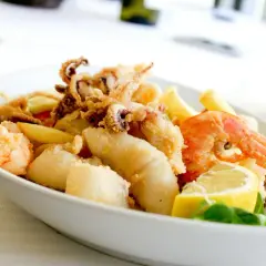 Knuspriges Fritto Misto mit Garnelen, Tintenfischringen und Fischstücken, garniert mit Zitrone und frischen Kräutern.
