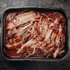 Saftiges pulled pork auf dem grill, in einer dunklen Schale mit BBQ-Sauce übergossen.