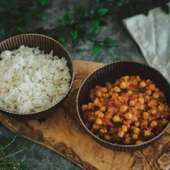 Schüssel mit Reis und eine Schüssel mit würzigem Chana Masala, serviert auf einem Holzbrett.