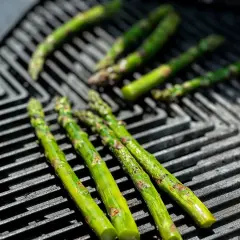Frischer Spargel grillen auf einem Gasgrill. Die grünen Stangen werden von der Hitze leicht gebräunt und verströmen ein köstliches Aroma.