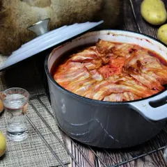 Herzhaftes Gericht in einem Topf, bedeckt mit Speckstreifen. Dazu Zwiebeln, Kartoffeln und ein Schnapsglas – typisch für russische Gerichte.