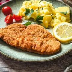 Knuspriges Putenschnitzel, mariniert und perfekt gegrillt, serviert mit Kartoffelsalat, Tomaten und Zitrone. Ein Genuss!