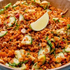 Ein Schüssel mit knusprigem Reis Salat, garniert mit Gurkenscheiben, Erdnüssen und Limettenspalten.