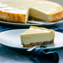 Ein Stück New York Cheesecake mit knusprigem Boden und cremiger Füllung auf einem Teller, daneben der ganze Kuchen.