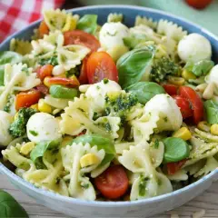 Ein bunter Nudelsalat mit Farfalle, Kirschtomaten, Mozzarella-Kugeln, Mais und frischem Basilikum, alles verfeinert mit einem köstlichen Pesto.
