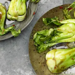 Zwei Teller mit gedünstetem Pak Choi, glänzend von einer Sauce und bestreut mit roten Chiliflocken.