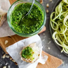 Frisches Basilikum-Pesto selber machen ist einfach! Hier ist ein Glas mit dem grünen Genuss, daneben Brot mit Pesto und eine Portion Spaghetti.