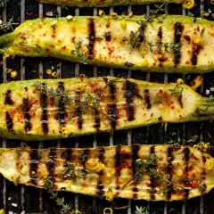 Perfekt gegrillte Zucchini-Scheiben mit Kräutern, Chili und Knoblauch auf dem Rost. Ein Genuss für jeden Grillmeister.