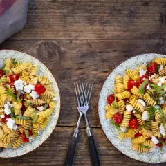 Zwei Teller mit leckeren schnellen Salaten ohne Mayo: Fusilli mit Kirschtomaten, Feta und Basilikum auf rustikalem Holztisch.