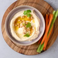 Cremiger Hummus mit Kichererbsen, Olivenöl und Petersilie, serviert mit Karotten- und Selleriesticks. Perfekt für ein schnelles Hummus Rezept.