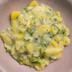 Ein cremiger Kartoffelsalat mit Speck, verfeinert mit frischer Petersilie und roten Zwiebeln, serviert in einer braunen Schale.
