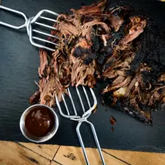 Zartes pulled beef mit dunkler Kruste, serviert mit BBQ-Sauce auf einem Schieferbrett.