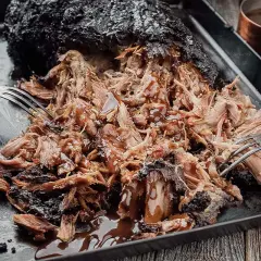 Saftiges Pulled Pork, frisch aus dem Smoker, mit einer dunklen Kruste und glänzender BBQ-Sauce. Zwei Gabeln zerreißen das Fleisch.