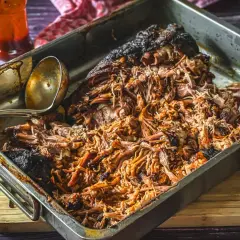Saftiges pulled pork, frisch aus dem Gasgrill, in einer Metallschale mit Sauce und Fleischgabel.
