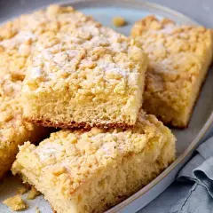 Saftiger Streuselkuchen vom Blech, mit Puderzucker bestäubt, auf einem Teller angerichtet.