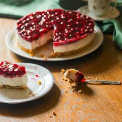 Ein köstlicher Kuchen ohne Backen mit Kirschtopping. Ein Stück auf einem Teller, ein Löffel mit einem Bissen daneben.