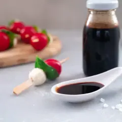 Ein Löffel mit dunkler balsamico creme, daneben eine Flasche und Radieschen-Mozzarella-Spieße.