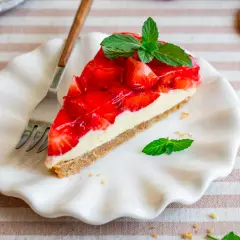 Ein Stück Erdbeerkuchen mit Keksboden, schnell und ohne Backen zubereitet. Frisch, fruchtig und mit Minze garniert.