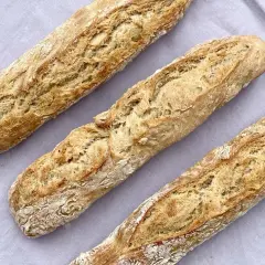 Drei frisch gebackene Baguettes mit knuspriger Kruste liegen auf einem grauen Tuch. Ein tolles Baguette Rezept zum Nachbacken!