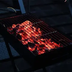 Glühende Kohlen unter dem Rost versprechen ein gemütliches Grillen mit Holzkohle. Funken tanzen in der Dunkelheit.
