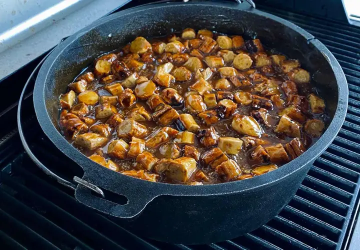 Leckere Currywurst-Stücke köcheln in einer würzigen Sauce in einem gusseisernen Dutch Oven auf dem Grill.