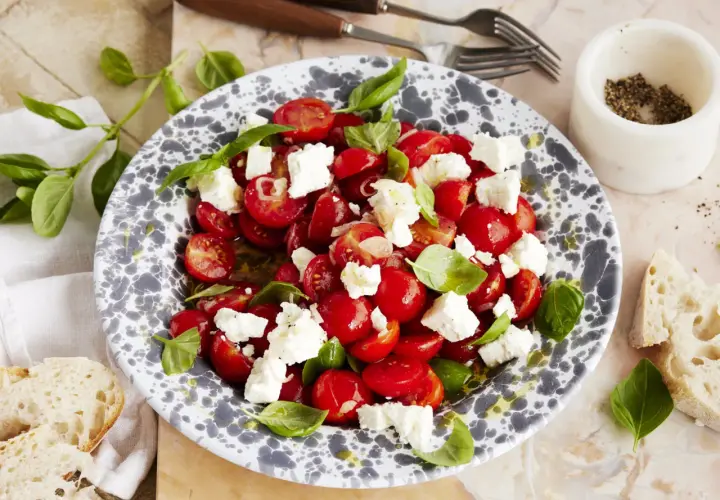 Frischer tomatensalat mit feta, garniert mit Basilikum. Dazu gibt es knuspriges Brot.
